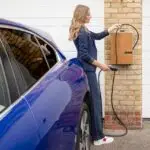 A woman efficiently charges her blue electric car at a home EV charging station.