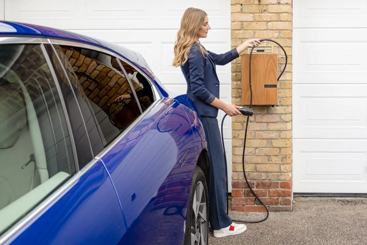 A woman efficiently charges her blue electric car at a home EV charging station.