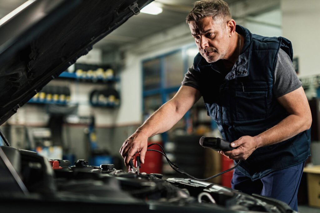 mecanicien d age moyen utilisant un outil de diagnostic tout en verifiant la tension d une batterie de voiture dans un atelier de reparation automobile