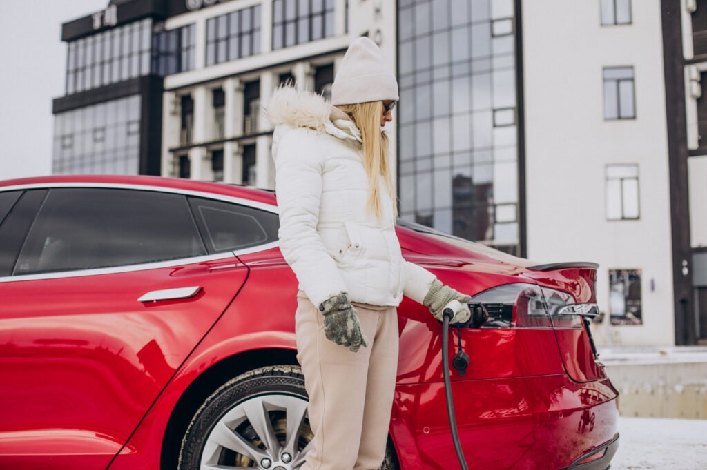 femme chargeant une voiture electrique rouge en hiver